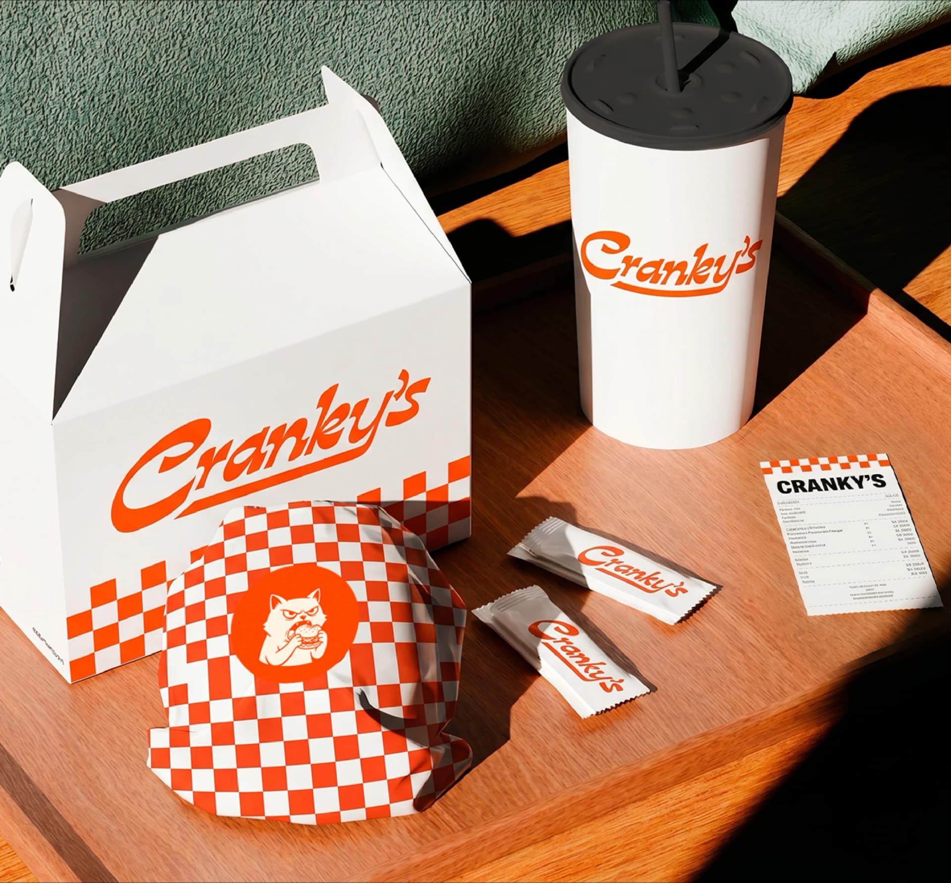 Cranky's packaging: a burger box, a cup, a checkerboard wrapper and sauce sachets